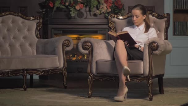 Young woman reading a book by fireplace. turns the pages — Stock Video
