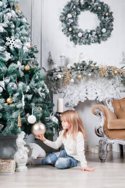 Sevimli küçük sarışın kız bir kot Noel ağacı yakınındaki bir katta oturan ve oyuncak üzerinde seyir olarak.