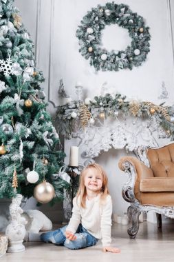 Sevimli küçük sarışın kız bir kot Noel ağacı yakınındaki bir katta oturan ve oyuncak üzerinde seyir olarak.