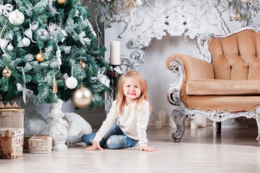 Sevimli küçük sarışın kız bir kot Noel ağacı yakınındaki bir katta oturan ve oyuncak üzerinde seyir olarak.