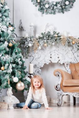 Sevimli küçük sarışın kız bir kot Noel ağacı yakınındaki bir katta oturan ve oyuncak üzerinde seyir olarak.