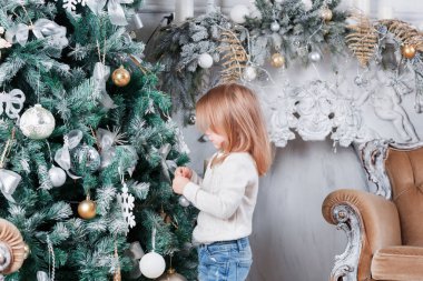 Sevimli küçük sarışın kız bir kot Noel ağacı yakınındaki bir katta oturan ve oyuncak üzerinde seyir olarak.
