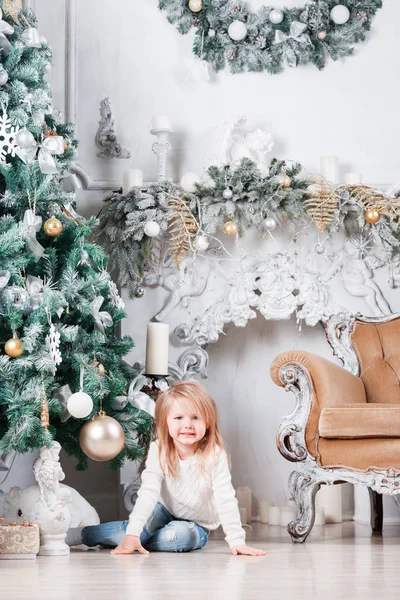 Sevimli küçük sarışın kız bir kot Noel ağacı yakınındaki bir katta oturan ve oyuncak üzerinde seyir olarak.
