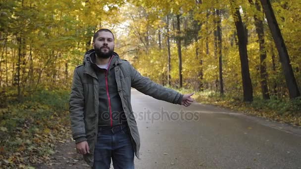 Caroneiro jovem com pé em uma estrada no outono. Conceito de aventura e turismo — Vídeo de Stock