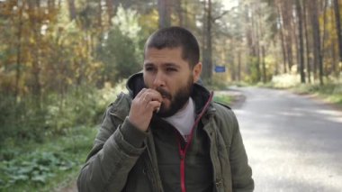 Orman güvenle bir sigara içen bir sonbaharda bir ceket giymiş genç yakışıklı adam izin duman.