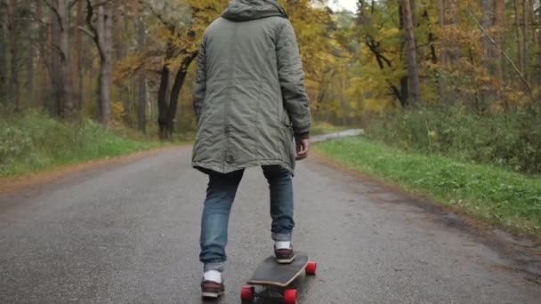 Homem montando em um skate de longboard em uma estrada através de uma floresta — Vídeo de Stock