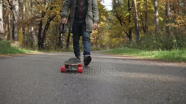 Homem montando em um skate de longboard em uma estrada através de uma floresta — Vídeo de Stock