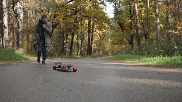 Homme chevauchant sur une planche à roulettes sur une route à travers une forêt — Video