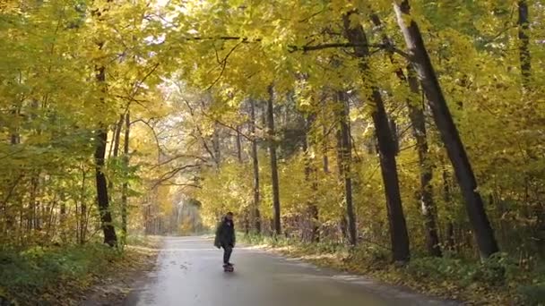 Человек едет на длинном коньке по дороге через лес — стоковое видео