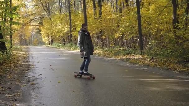 Man ridande på en longboard skridsko på en väg genom en skog — Stockvideo