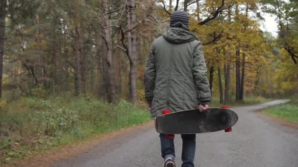 Man ridande på en longboard skridsko på en väg genom en skog — Stockvideo