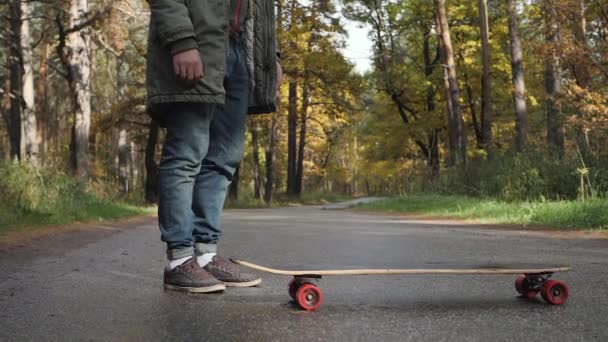 Man riding on a longboard skate on a road through a forest — Stock Video