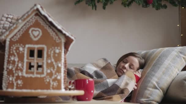 毛布の下のソファに横たわっています。一杯のお茶で病気にかかった女性の健康と病気概念。クリスマスの朝. — ストック動画
