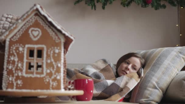 毛布の下のソファに横たわっています。一杯のお茶で病気にかかった女性の健康と病気概念。クリスマスの朝. — ストック動画