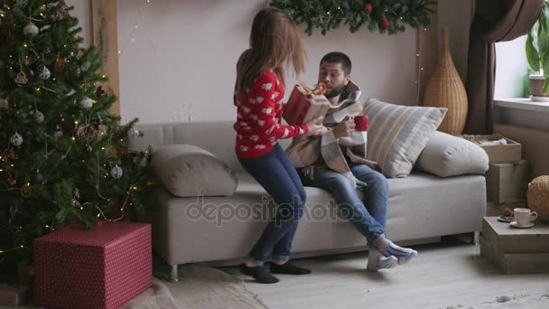 Belo jovem casal está comemorando em casa. Menina bonita está dando seu namorado uma caixa de presente — Vídeo de Stock