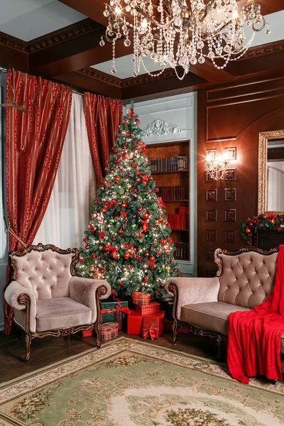 Christmas evening. classic apartments with a white fireplace, decorated tree, sofa, large windows and chandelier.