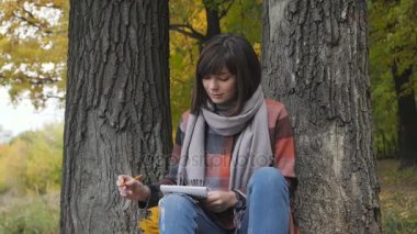 Harika sonbahar görünümü. Büyüleyici genç mutlu bir parkta çimlerde oturan kadın gülümsüyor not not defterinde almak.