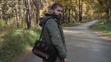 Yakışıklı delikanlı bir sonbahar ormanda yürüyüş bir ceket giymiş. Parkta niteliğine portre. Ormanda yolda hareket