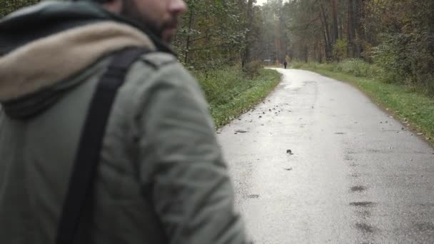 Ein junger gutaussehender Mann in einer Jacke, der in einem herbstlichen Wald spazieren geht. Porträt über die Natur des Parks. Umzug auf der Waldstraße — Stockvideo