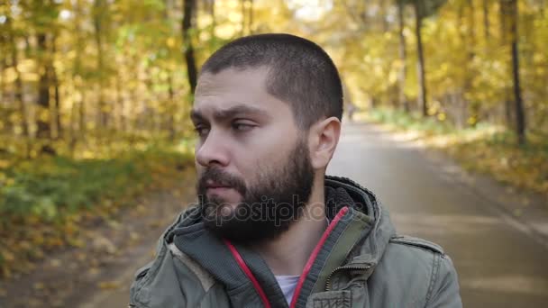 Joven hombre guapo vestido con una chaqueta caminando en un bosque de otoño. Retrato sobre la naturaleza del parque. Muévete por el camino del bosque — Vídeo de stock