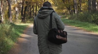 Yakışıklı delikanlı bir sonbahar ormanda yürüyüş bir ceket giymiş. Parkta niteliğine portre. Ormanda yolda hareket
