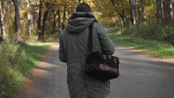 Homem bonito jovem vestido com uma jaqueta andando em uma floresta de outono. Retrato sobre a natureza do parque. Mova-se na estrada da floresta — Vídeo de Stock