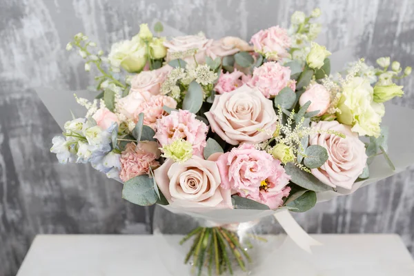 Hermoso ramo de flores mezcladas en un jarrón en la mesa de madera. el trabajo de la floristería en una florería. envoltura de plástico esmerilado — Foto de Stock