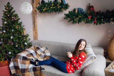 Mutlu kız izlerken akış içeriği kışın evde bir kanepede oturan bir akıllı telefon bir satır