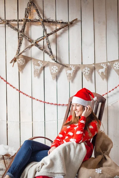 Celebração de Natal ou Ano Novo. Mulher feliz sentada na cadeira de balanço. olhando para o lado. o chapéu de Papai Noel — Fotografia de Stock