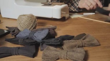 hazır yapılmış kelebek papyon yün ön planda, yapılan bir sürü bir bitmiş ürün ekler. Bir terzi çalışan ve bir dikiş makinesi bir tekstil Studio'yu kullanarak iyi görünümlü genç adam.