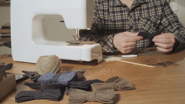 Lotes de laços borboleta pronto feito de lã em primeiro plano, acrescenta um produto acabado. Jovem bem parecido trabalhando como alfaiate e usando uma máquina de costura em um estúdio têxtil . — Vídeo de Stock