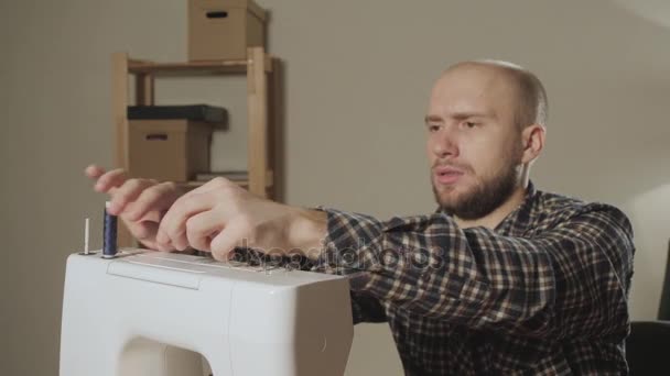 Jovem homem define o carretel de linha na máquina. Trabalhando como alfaiate e usando uma máquina de costura em um estúdio têxtil. faz laços de arco — Vídeo de Stock