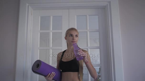 Heimfitness. Sauberes Wasser aus der Flasche trinken. junge Frau beim Training. in der Nähe vom Fenster — Stockvideo