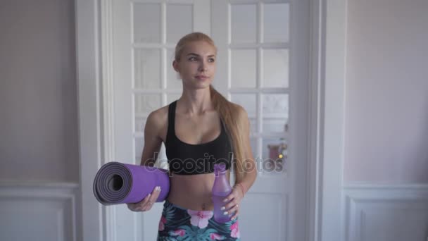 Hem fitness. Drick rent vatten från en flaska. Ung kvinna utbildning gör. nära fönstret — Stockvideo