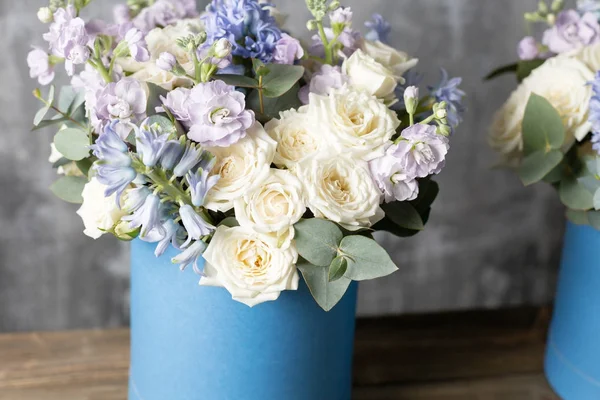 Deux bouquets de fleurs dans une boîte à chapeau bleu. debout sur une table en bois. Sur le fond vieux mur gris art. espace de copie . — Photo
