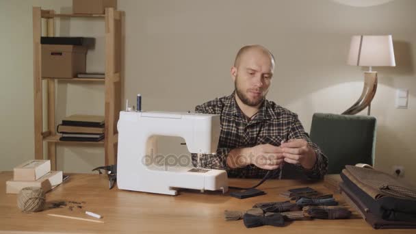 Fait des noeuds papillon. Jeune homme travaillant comme tailleur et utilisant une machine à coudre dans un atelier textile . — Video