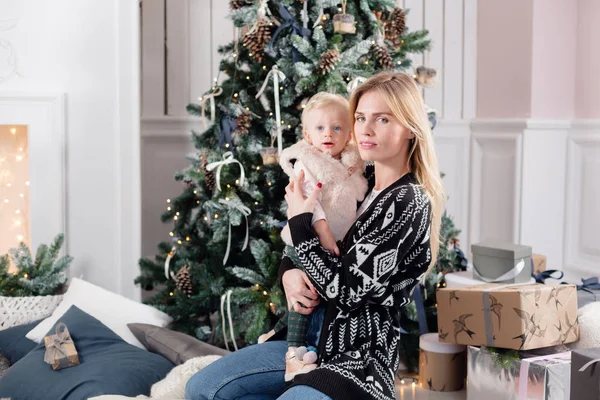 Vánoční a silvestrovské oslavy. Šťastný matka a dcera objímat poblíž vánoční stromeček s vánočními dárky. Bílé krb na pozadí — Stock fotografie