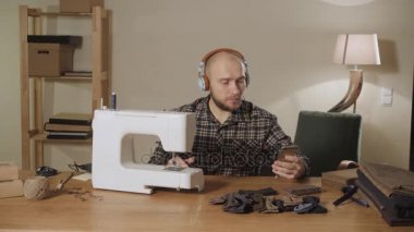 genç adam kulaklık takıyor ve müzik dinliyor. Bir terzi çalışan ve bir dikiş makinesi bir tekstil Studio'yu kullanarak. papyon yapar