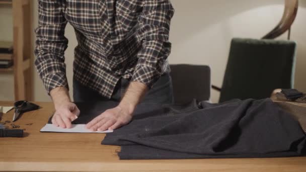 Snijden wollen stof. het lijnpatroon. Strikjes van wollen weefsel. Jonge man werken als een kleermaker en een naaimachine gebruiken in een textiel-studio. — Stockvideo