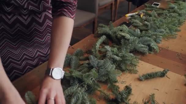 Florista no trabalho: mãos de mulher que fazem decorações de Natal grinalda de abeto Nobilis. Feliz ano novo jantar festa — Vídeo de Stock