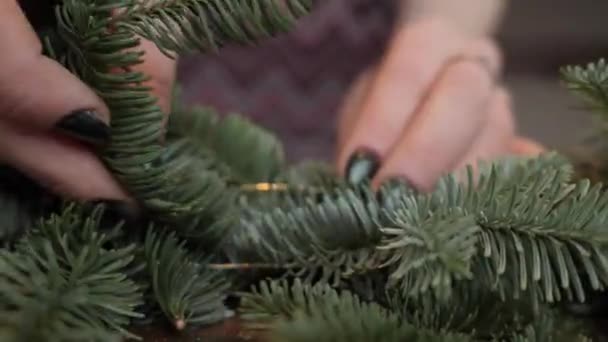 Primer plano de la mano. Florista en el trabajo: manos de mujer haciendo adornos navideños guirnalda de abeto Nobilis. Feliz año nuevo cena fiesta — Vídeo de stock