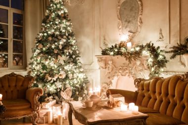 Noel akşam mum ışığında. Klasik dairelerde beyaz bir şömine, dekore edilmiş ağaç, kanepe, büyük pencereler ve avize.