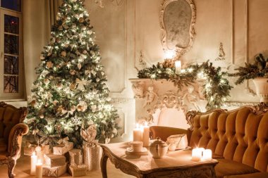 Noel akşam mum ışığında. Klasik dairelerde beyaz bir şömine, dekore edilmiş ağaç, kanepe, büyük pencereler ve avize.