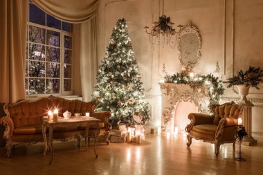 Noel akşam mum ışığında. Klasik dairelerde beyaz bir şömine, dekore edilmiş ağaç, kanepe, büyük pencereler ve avize.