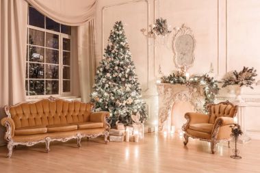 Noel akşam mum ışığında. Klasik dairelerde beyaz bir şömine, dekore edilmiş ağaç, kanepe, büyük pencereler ve avize.