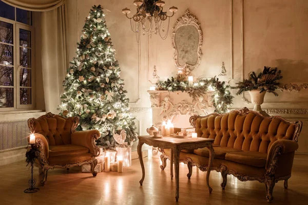 Christmas evening by candlelight. classic apartments with a white fireplace, decorated tree, sofa, large windows and chandelier. — Stock Photo, Image