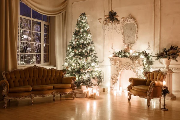 Heiligabend bei Kerzenschein. klassische Appartements mit weißem Kamin, geschmücktem Baum, Sofa, großen Fenstern und Kronleuchter. — Stockfoto