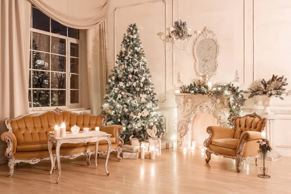 Vánoční večer při svíčkách. Klasické apartmány s bílým krbem, nazdobený stromeček, pohovka, velkými okny a lustr. — Stock fotografie