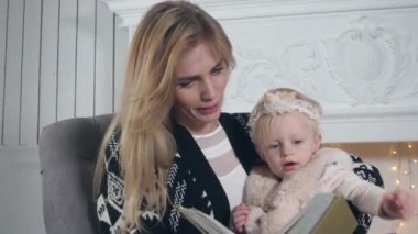 kitabı oku. Mutlu anne ve kızı kucaklayan. Şömine ve dekore edilmiş ağaç arka plan üzerinde beyaz. Noel ve yeni yıl kutlama.