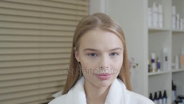 Portrait d'une jolie femme souriante blonde. Dans un peignoir blanc après la procédure. Concept de centre de cosmétologie et SPA . — Video